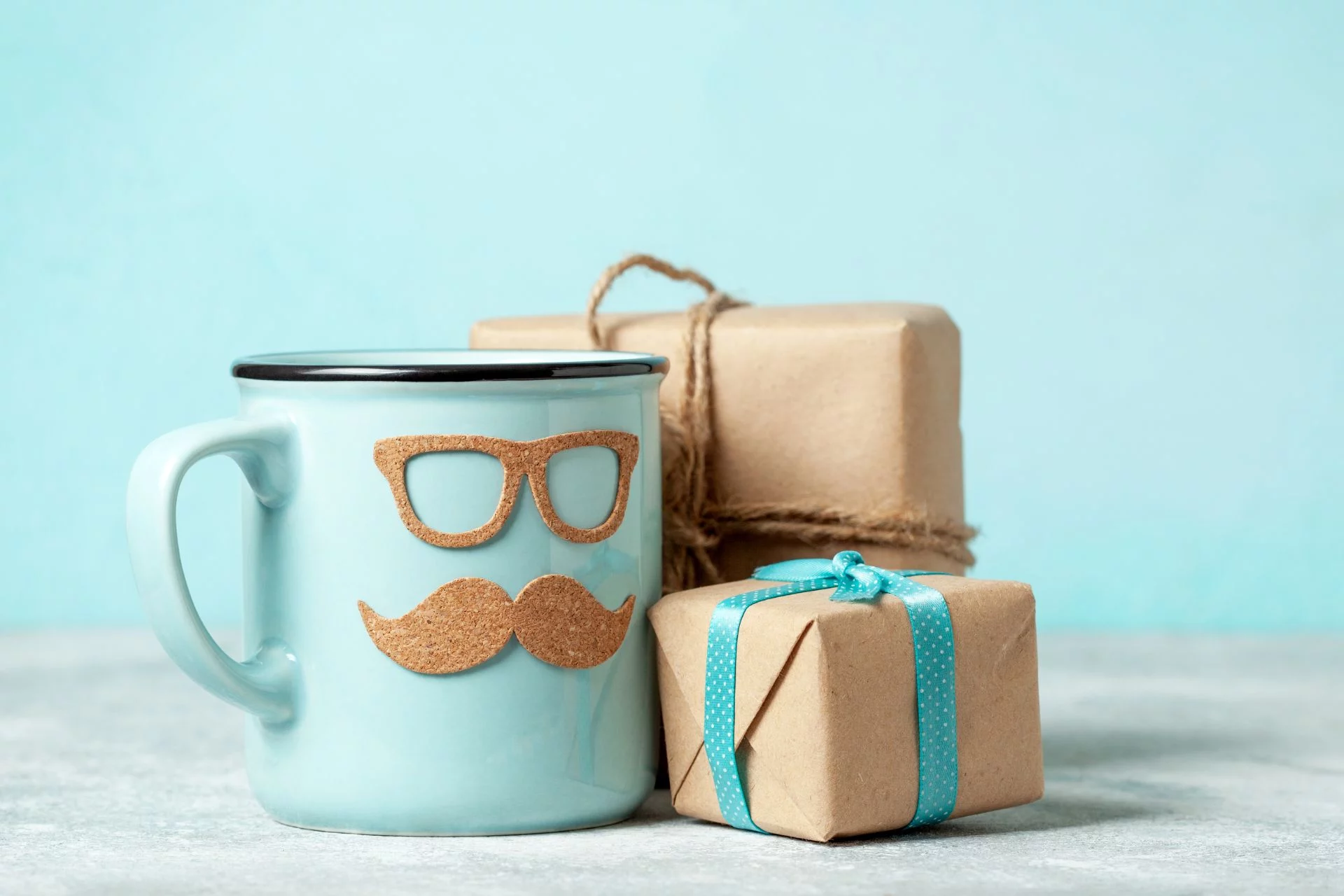 Caneca azul com óculos de nerd e bigode ao lado de dois presentes em papel kraft